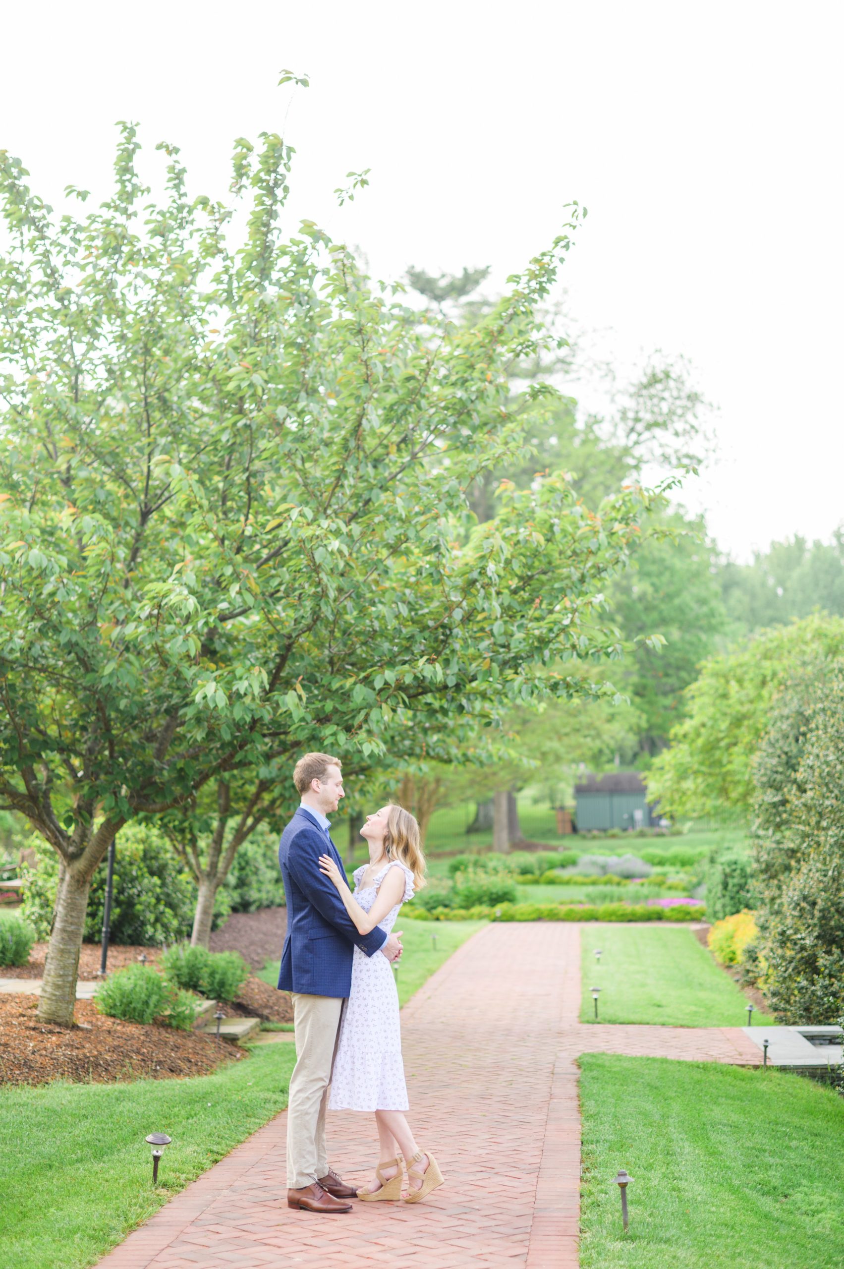 Engaged Couple smiles in the garden at Belmont Manor during a rainy sunset engagement photographed by Baltimore Wedding Photographer Cait Kramer