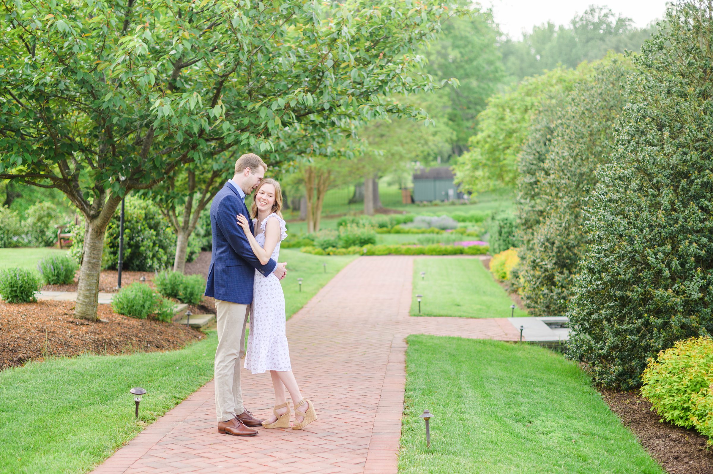 Engaged Couple smiles in the garden at Belmont Manor during a rainy sunset engagement photographed by Baltimore Wedding Photographer Cait Kramer