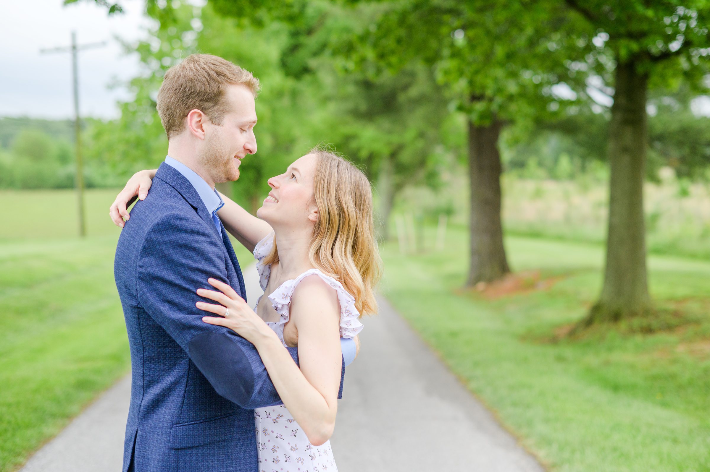 Engaged Couple poses on the treelined driveway at Belmont Manor during a rainy sunset engagement photographed by Baltimore Wedding Photographer Cait Kramer