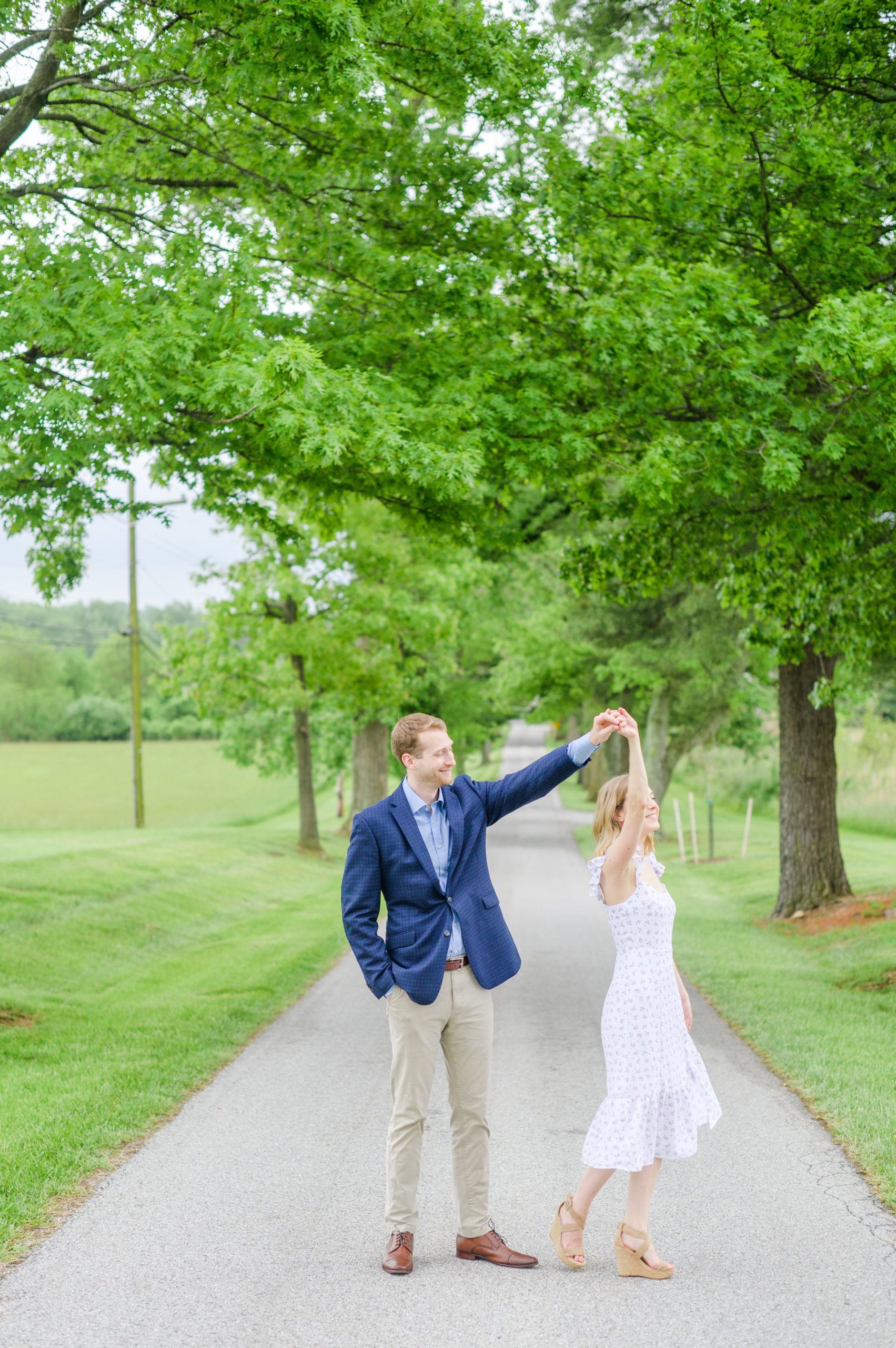 Engaged Couple poses on the treelined driveway at Belmont Manor during a rainy sunset engagement photographed by Baltimore Wedding Photographer Cait Kramer