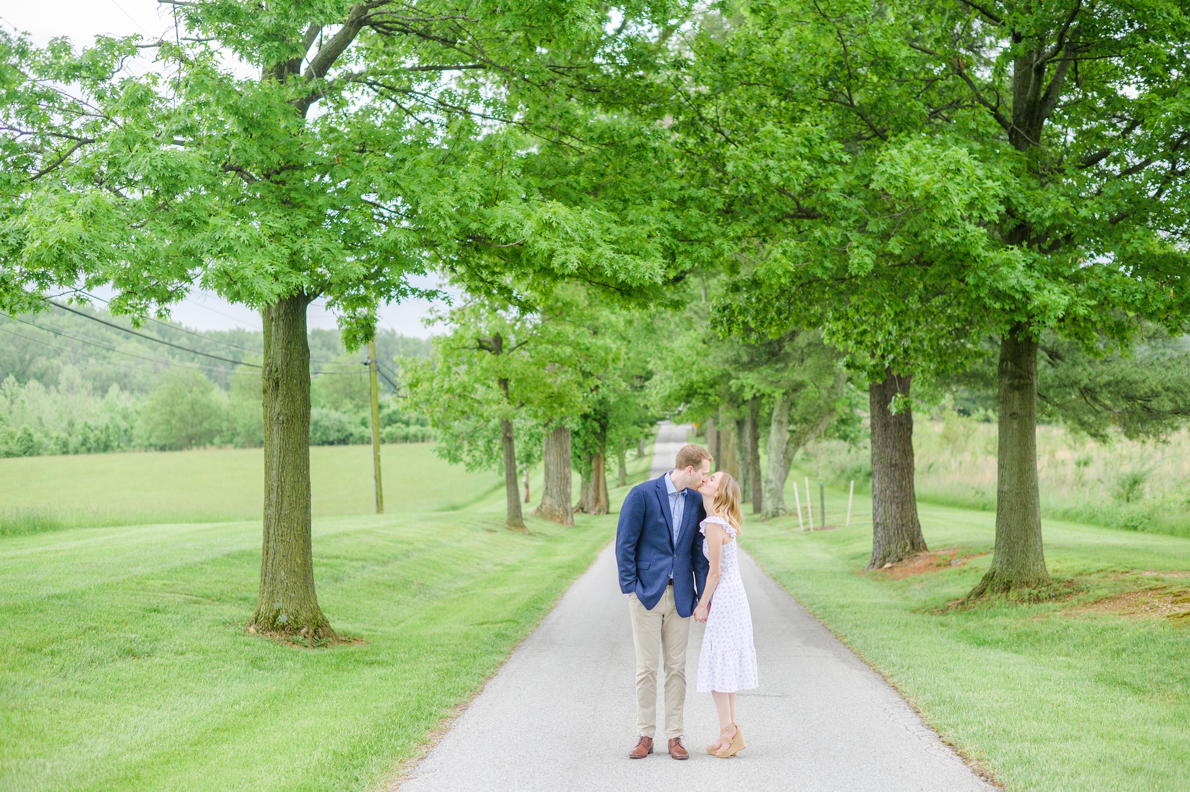Engaged Couple poses on the treelined driveway at Belmont Manor during a rainy sunset engagement photographed by Baltimore Wedding Photographer Cait Kramer