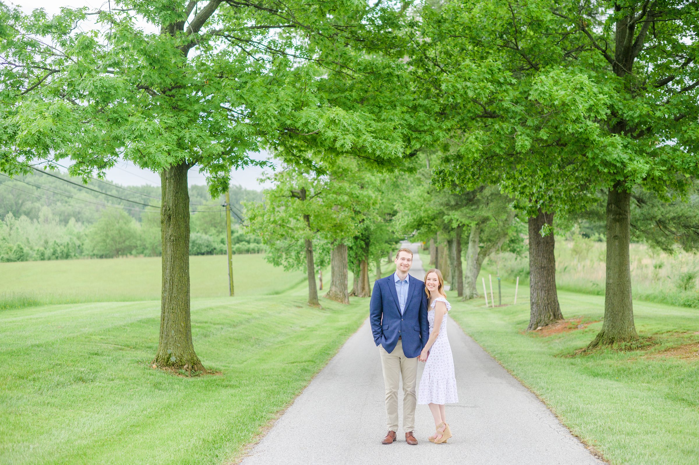 Engaged Couple poses on the treelined driveway at Belmont Manor during a rainy sunset engagement photographed by Baltimore Wedding Photographer Cait Kramer