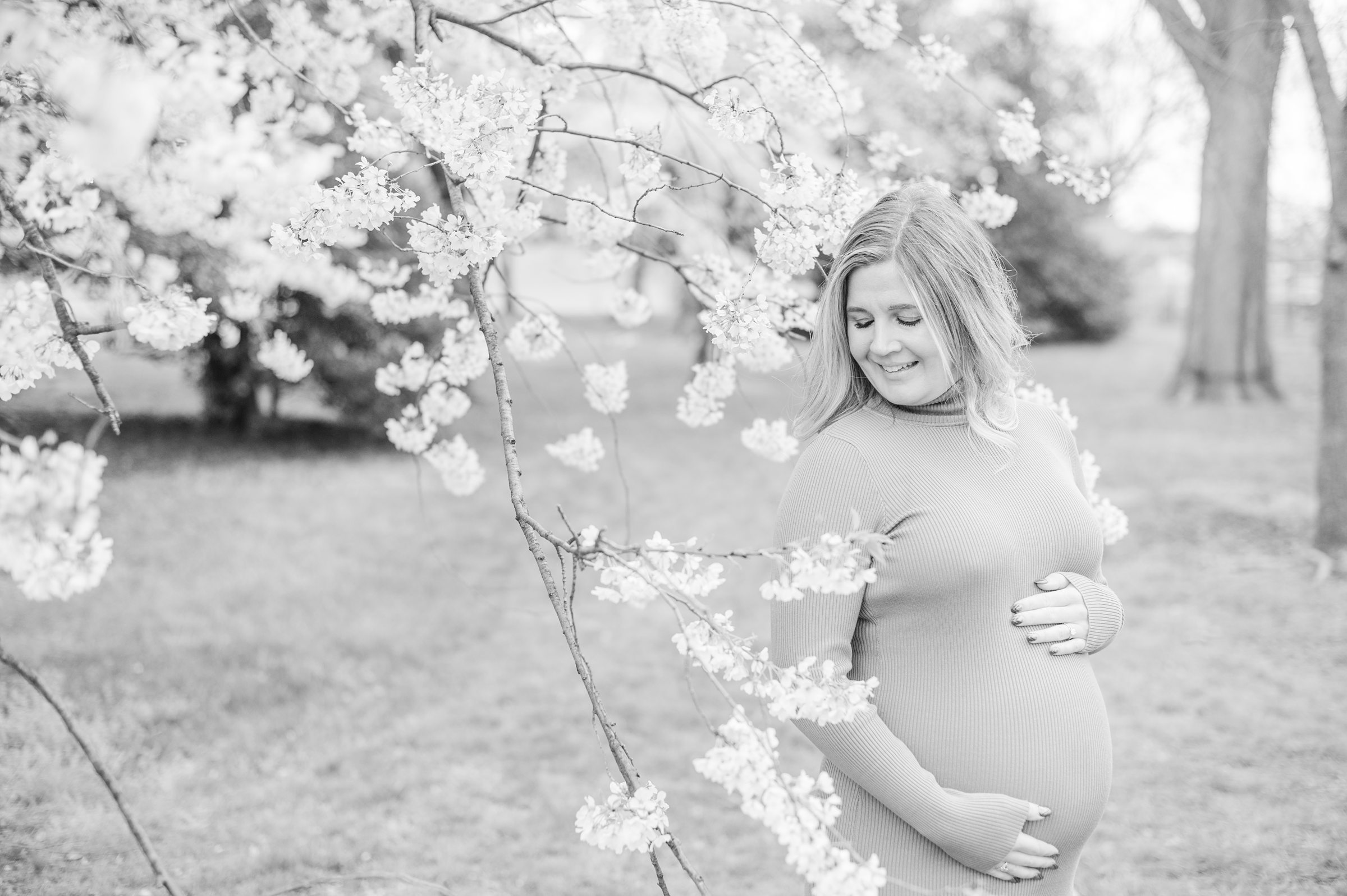 Mama-to-be poses with her bump amongst the cherry blossoms at the Washington, DC Tidal Basin during a maternity session photographed by Cait Kramer Photography