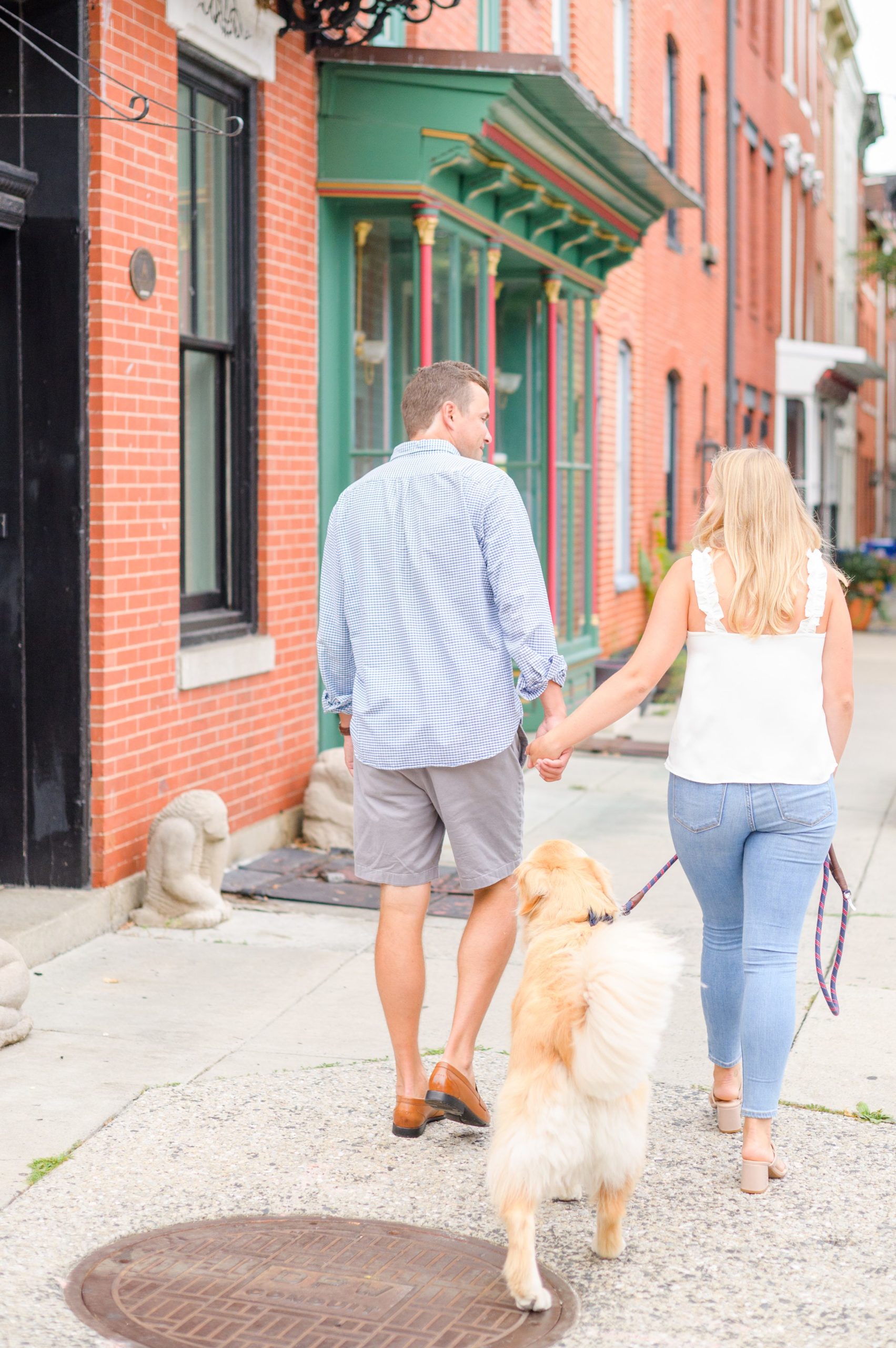 Couple walks through their neighborhood with their dog during Fells Point engagement session photographed by Baltimore wedding photographer Cait Kramer