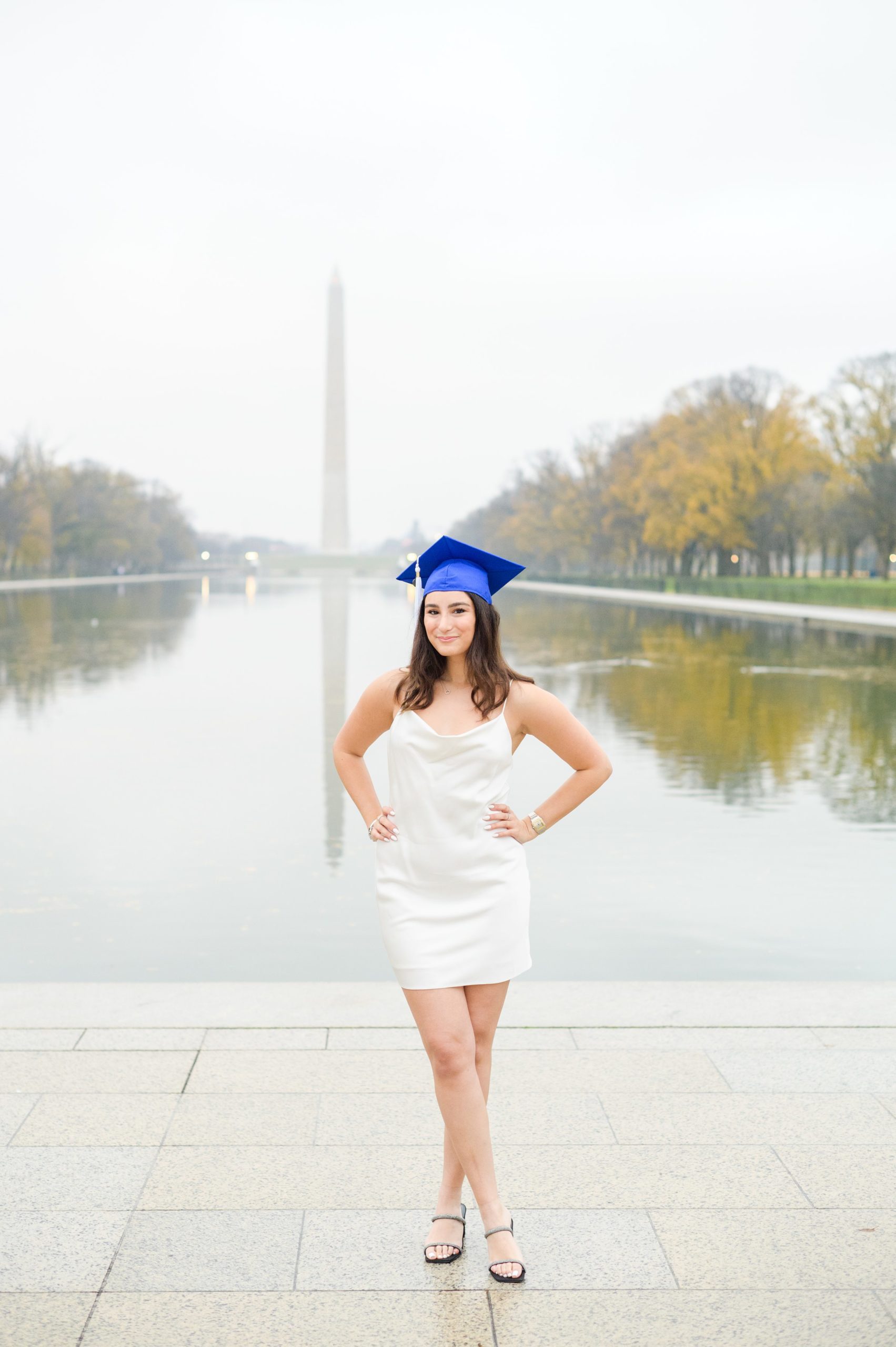 American University senior poses at the Lincoln Memorial in graduation attire during Washington DC Grad Session photographed by Cait Kramer