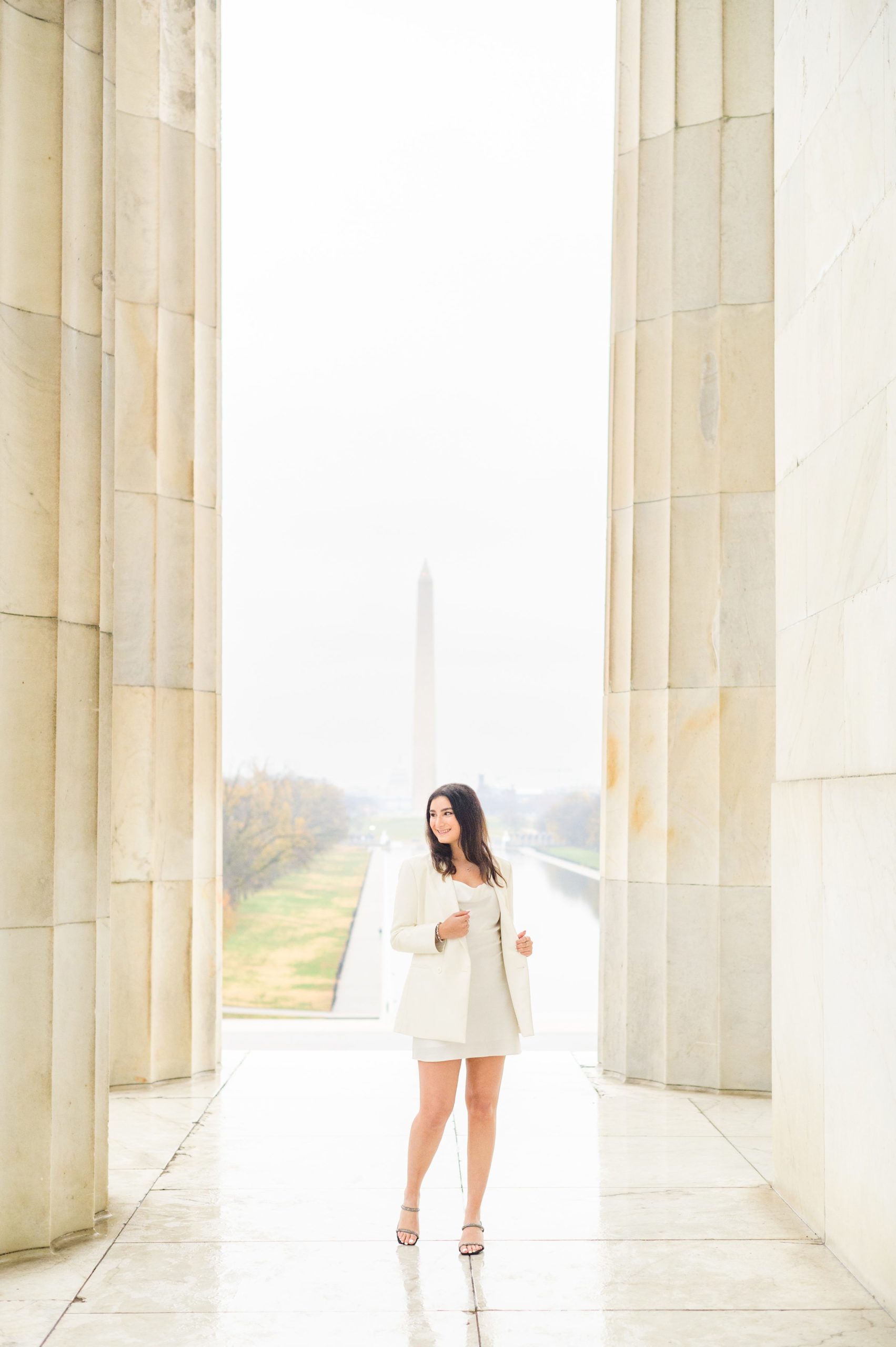 American University senior poses at the Lincoln Memorial in graduation attire during Washington DC Grad Session photographed by Cait Kramer