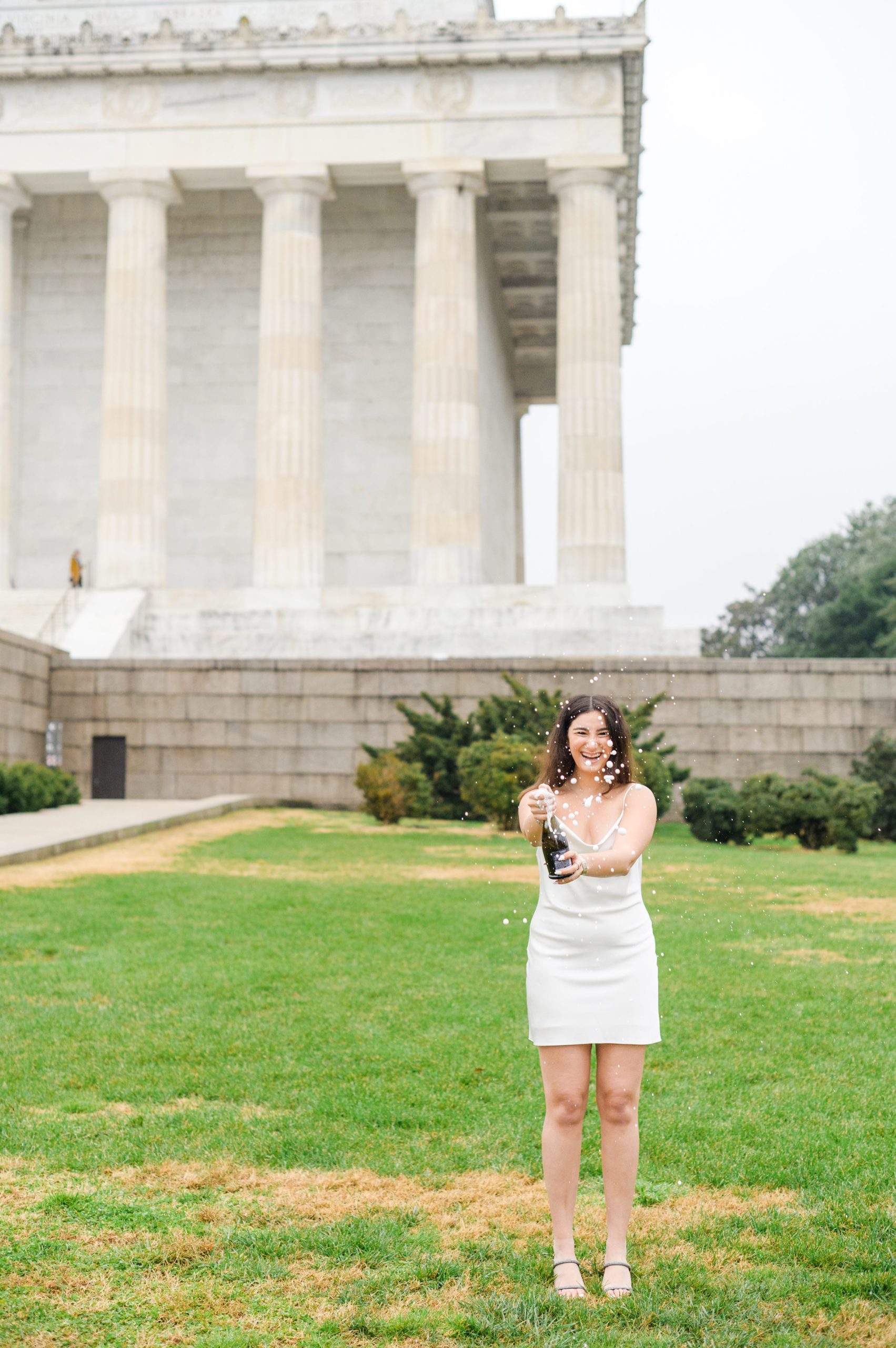 American University senior poses at the Lincoln Memorial in graduation attire during Washington DC Grad Session photographed by Cait Kramer