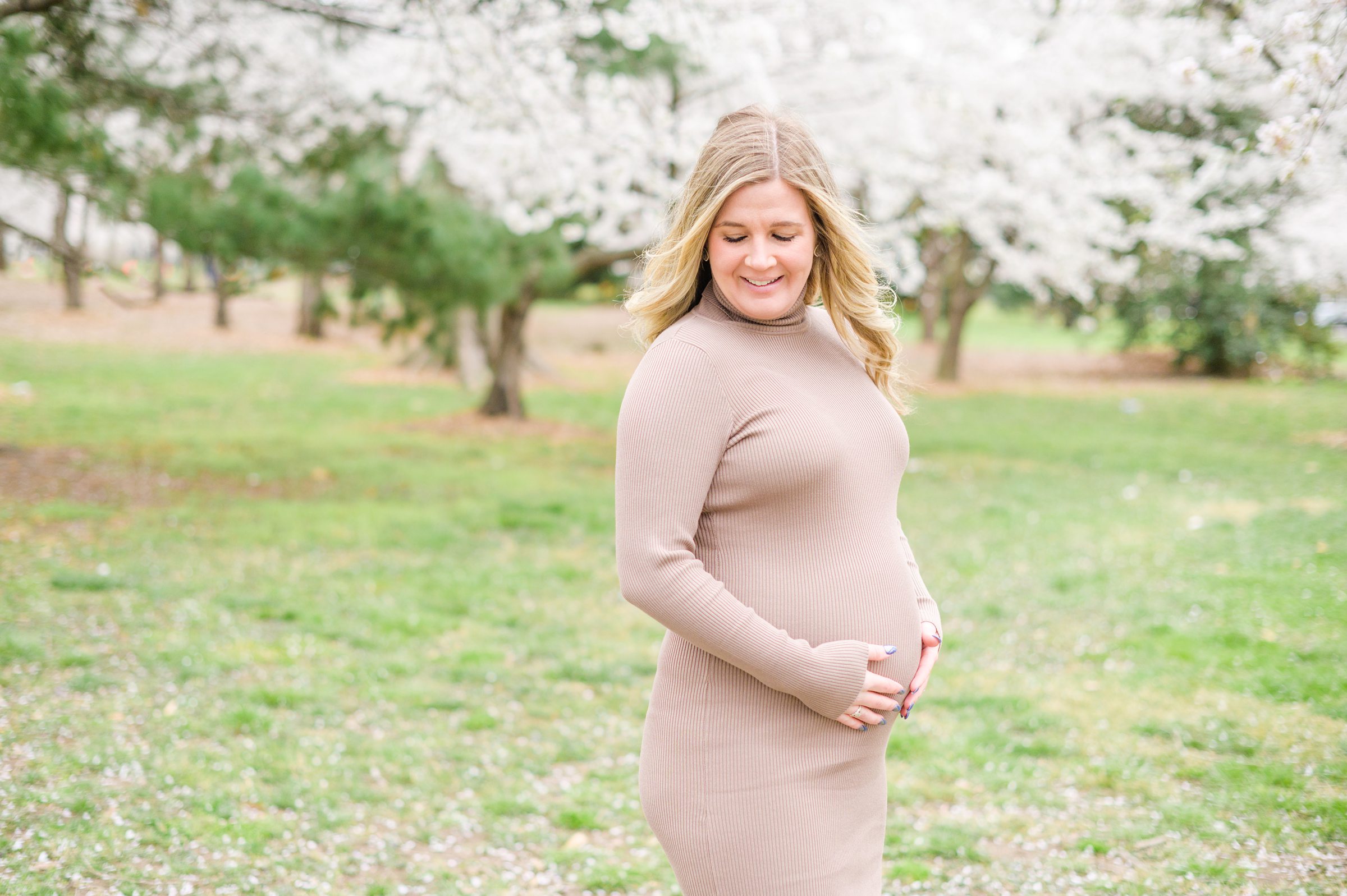 Mama-to-be poses with her bump amongst the cherry blossoms at the Washington, DC Tidal Basin during a maternity session photographed by Cait Kramer Photography