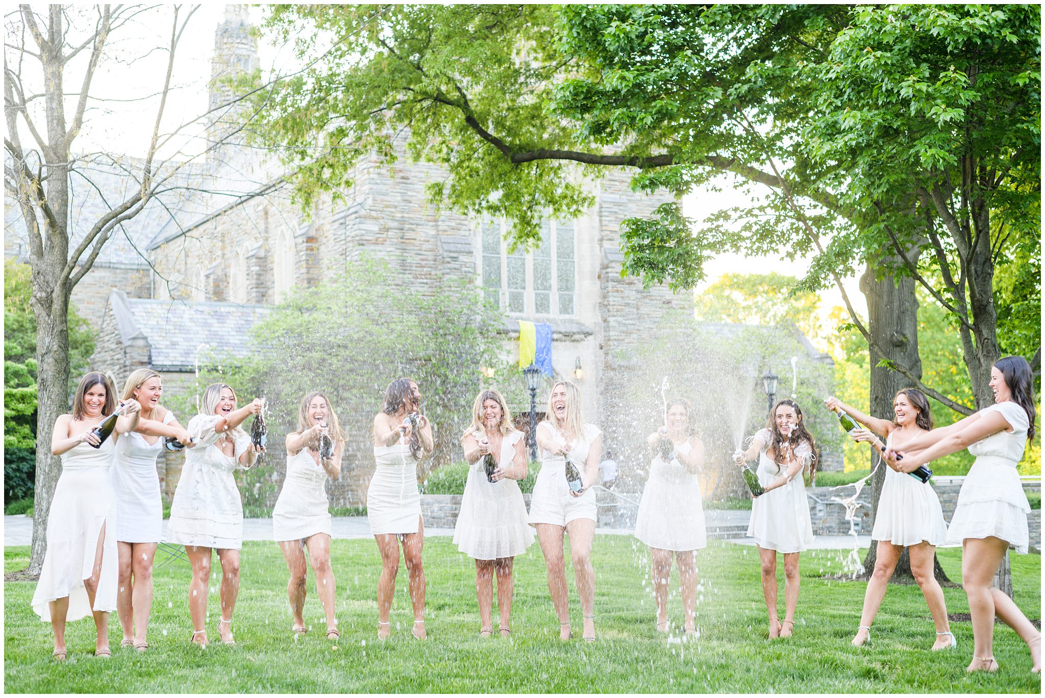 College graduates pop champagne bottles in white dresses photographed by Baltimore Photographer Cait Kramer